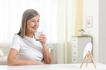 Smiling woman drinking collagen water at table indoors