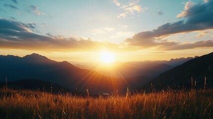 Obraz premium Majestic sunset over a mountain range, casting a golden glow on the tall grass in the foreground. The sun's rays illuminate the peaks and valleys, creating a breathtaking landscape. : Generative AI