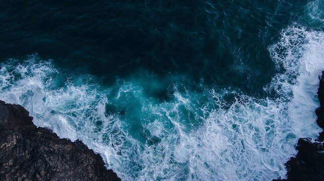 Aerial view of ocean waves crashing against dark rocks, showcasing a dramatic contrast between the white foam and deep teal water. The image evokes a sense of power and the untamed bea : Generative AI
