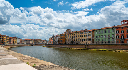 Fototapeta premium City center of Pisa, Italy, with the Arno River flowing through. Colorful riverside buildings line the banks under bright summer skies in a warm Mediterranean atmosphere.