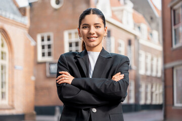 Attractive young woman realtor in sleek black suit stands confidently on city street, ideal for real estate branding, urban professionalism, career empowerment, or modern leadership