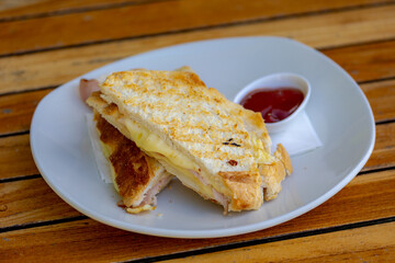 Toasted ham and cheese sandwich in white plastic plate served with tomato ketchup sauce on the side, The tosti in Netherlands or croque-monsieur is a hot sandwich made with ham and cheese.
