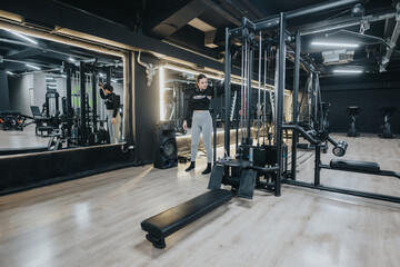 Fototapeta premium A woman exercises in a well-lit, modern fitness center, utilizing various gym machines and equipment, promoting a healthy lifestyle and physical activity. Reflection in mirrors adds a dynamic element