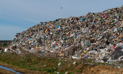 Massive landfill brimming with waste material, showing a mountain of garbage under blue sky,...