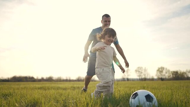 Father and son playing soccer in the field. Soccer field with adult child playing on grass outside. Father running through a field of trees with a ball rassing sunlight. A father and his lifestyle.