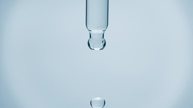 Cosmetics blue liquid dripping from laboratory glass pipette in super slow motion. Macro shot of drop hanging down from chemical dropper. Abstract body care serum ingredients formulating concept