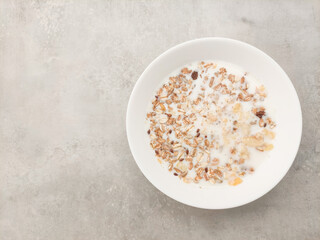 Creamy bowl of nutritious breakfast cereal topped with crunchy oats and flakes in milk on textured surface