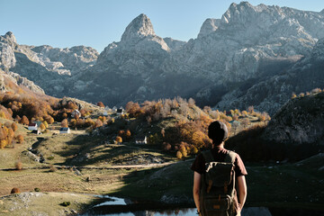 Female solo hiker with a backpack admires the majestic peaks of Montenegro in warm autumn light....