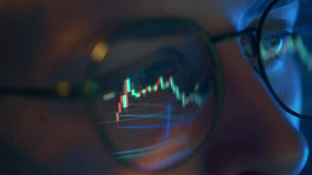 Trader wearing glasses is working on laptop computer. Screen with stock market charts and Bitcoin BTC or Ethereum ETH data analysis reflection. Broker trading online. Altcoins crypto currency trading