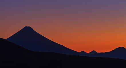Dramatic mountain silhouette against vibrant sunset sky with gradient from deep purple to bright orange. Natural wonder. Landscape, sunset tours, meditation retreats, posters, adventure tourism