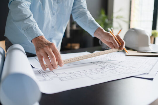 Close up of female architect sitting at her office desk and working with blueprints cadastral maps city plans. Mature Caucasian woman studying information and developing a new architectural project