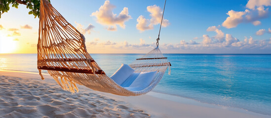 Empty hammock hanging between two palm trees on tropical beach at sunset