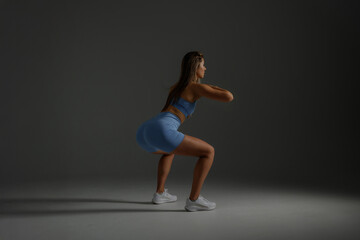 Obraz premium Young woman performing squats in a fitness studio with dim lighting and neutral background for strength training