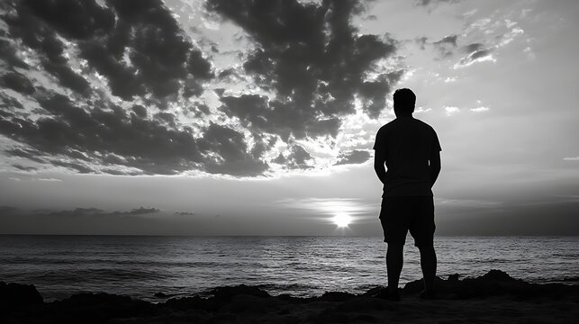 Silhouette of a man standing on a rocky shore, gazing at a dramatic sunset over a calm ocean, under a sky filled with dark, brooding clouds. : Generative AI - Powered by Adobe