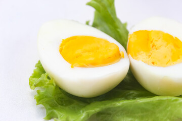 close up of halved boiled egg on lettuce leaf isolated on white background