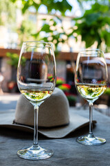 Two elegant glasses of white wine sit beside a fashionable hat in a sunny outdoor setting