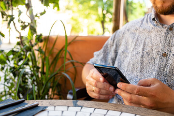 A person at a sunny cafe, engrossed in their smartphone among the greenery