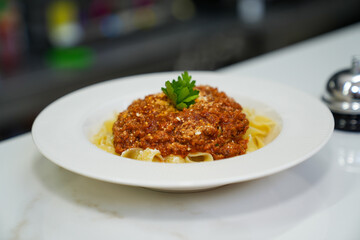 Top view of fettuccine pasta with tomato sauce, cheese and parsley on a white plate on a table.