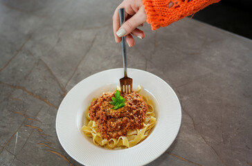 Close up view of eating pasta with tomato sauce, and parsley with a fork.