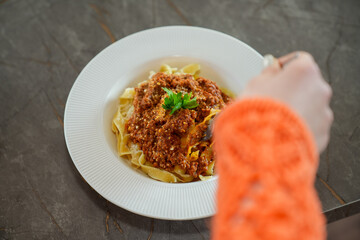 Close up view of eating pasta with tomato sauce, and parsley with a fork.