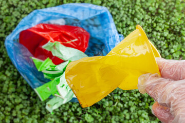 Hand holding crumpled plastic cup on the background is filled with small, green sprouts. Plastic waste against a background of green plants - environmental pollution. Garbage collection process