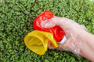 Hand holding two crumpled plastic cups on The background is filled with small, green sprouts. Plastic waste against a background of green plants - environmental pollution. Garbage collection process