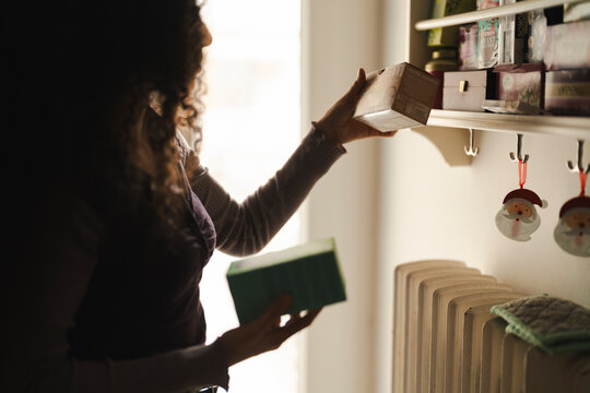 An Arab woman with curly dark hair is taking a box from a shelf. She is organizing the pantry in her home.