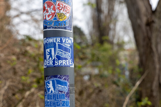 Close-up of a pole covered in Hertha BSC Berlin football club stickers and graffiti, showing fan culture