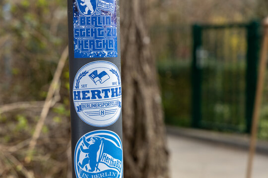 Close-up of a black pole covered in blue and white Hertha BSC football club stickers logo, showing fan support.