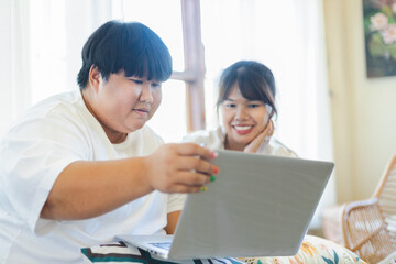 Obraz premium Asian couple enjoys relaxed lifestyle together using laptop for indoor activity filled with warmth and connection