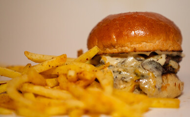 Close up view of french fries and hamburger with meat, mushroom, sauce, and melted cheese isolated on white background.