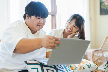 Asian couple enjoys relaxed lifestyle together using laptop for activity at home with warm natural light and happy expressions