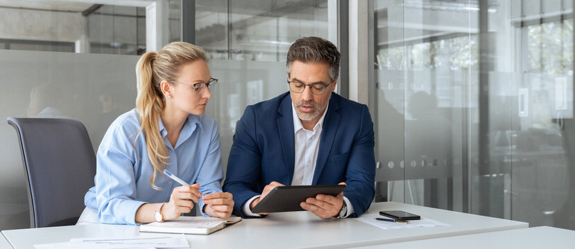 Team leader explain trainee working process using tablet pc computer. Two professional business people working together. Partners mature man, woman discussing project in office workplace. Copy space