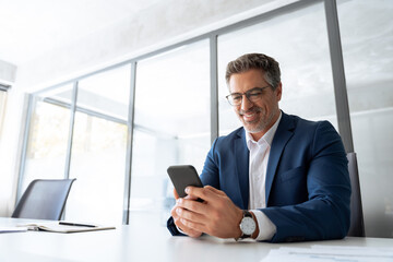 Fototapeta premium Professional businessman senior manager using mobile cellphone telephone application for communication at work at office workplace. Smiling mature executive trader man in suit working on device online