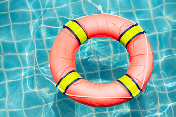 Red lifebuoy floating on blue water in the pool and copy space.Emergency help and safety equipment.Life buoy ring lifebelt for accident prevention water rescue.Rescue water concept.