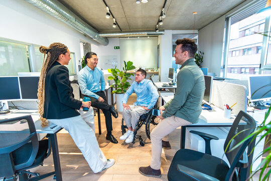 Diverse business team discussing in modern office with disabled colleague in wheelchair