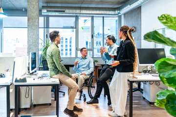 Diverse business team discussing project in modern office with disabled colleague in wheelchair