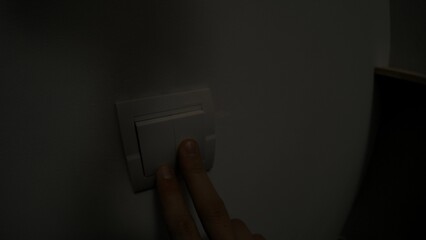 Finger Pressing Light Switch on a Plain Wall Surface