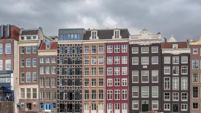 Hyperlapse of colorful Canal Houses on Damrak in evening light, reflected in water with boats passing by under dramatic clouds timelapse. A charming view of Amsterdam, Netherlands