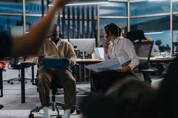 Fototapeta premium Multicultural colleagues working together on a project at night, focusing on meeting their deadline. The collaboration highlights diversity, teamwork, and dedication in a dynamic office environment.