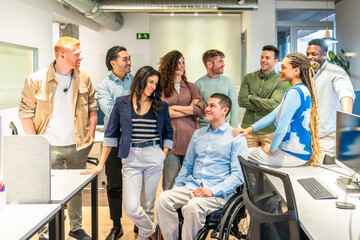 Diverse business team supporting disabled colleague in wheelchair at modern office