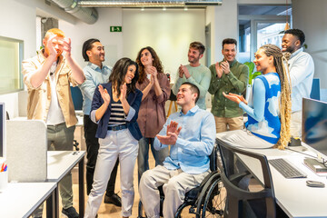 Diverse business team clapping and celebrating success in modern office with disabled colleague