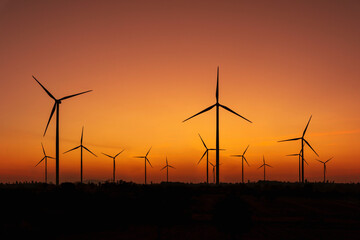 Silhouette of wind turbines farm with beautiful orange during sunset. Clean energy, alternative energy for the future