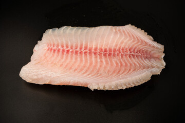 Fresh tilapia fillet on black background, top view.