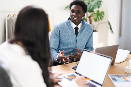 Two colleagues are collaborating on a project in a bright, modern office. They are using laptops and discussing ideas, with one person gesturing to emphasize a point.