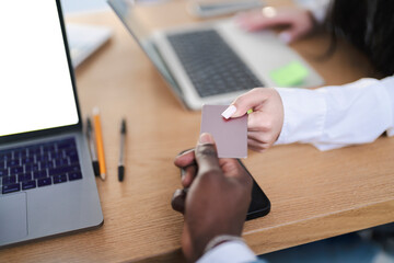 A woman hands a business card to a man. They are at a desk with laptops and pens. It could be a meeting or networking event.