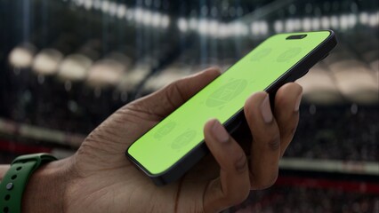 GREEN SCREEN CHROMA KEY A hand holding a phone with a green screen at a stadium during a football...