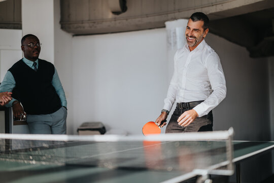 Multicultural business workers enjoying a fun break at the office, playing table tennis and relaxing. The workplace atmosphere is casual and friendly, highlighting teamwork and work-life balance. - Powered by Adobe