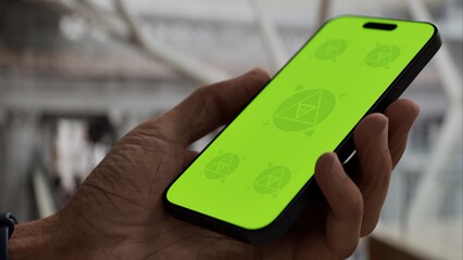 GREEN SCREEN CHROMA KEY Person holding a smartphone with a green screen in a spacious indoor area featuring modern architecture and hardwood flooring