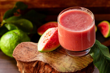 Delicious red guava juice alongside a slice of guava, in the background guavas and leaves on rustic...